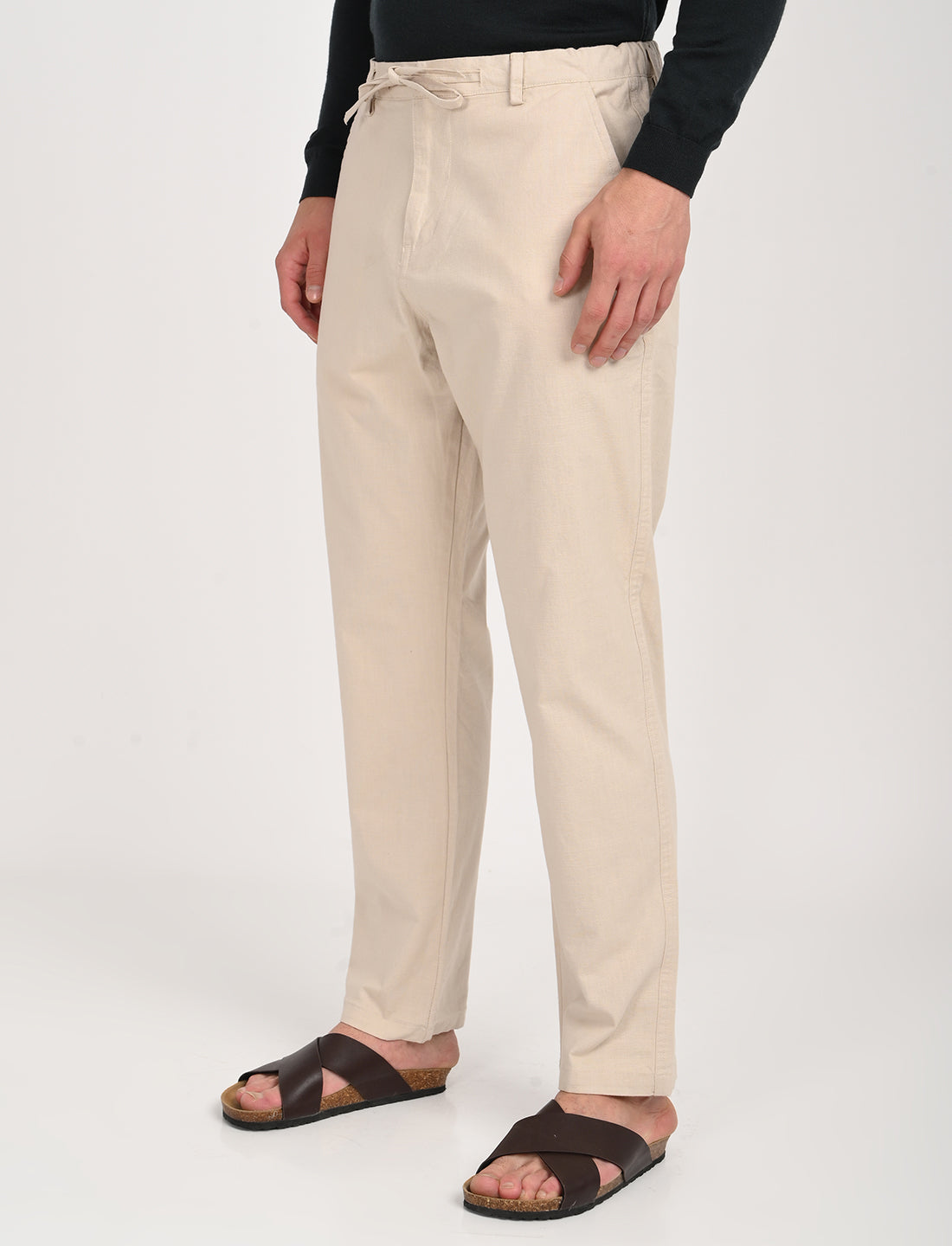 Men's cream linen blend trousers with a relaxed fit, worn with sandals for a casual look.