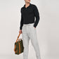 Model wearing light grey linen blend trousers with black long-sleeve polo and holding a green bag.